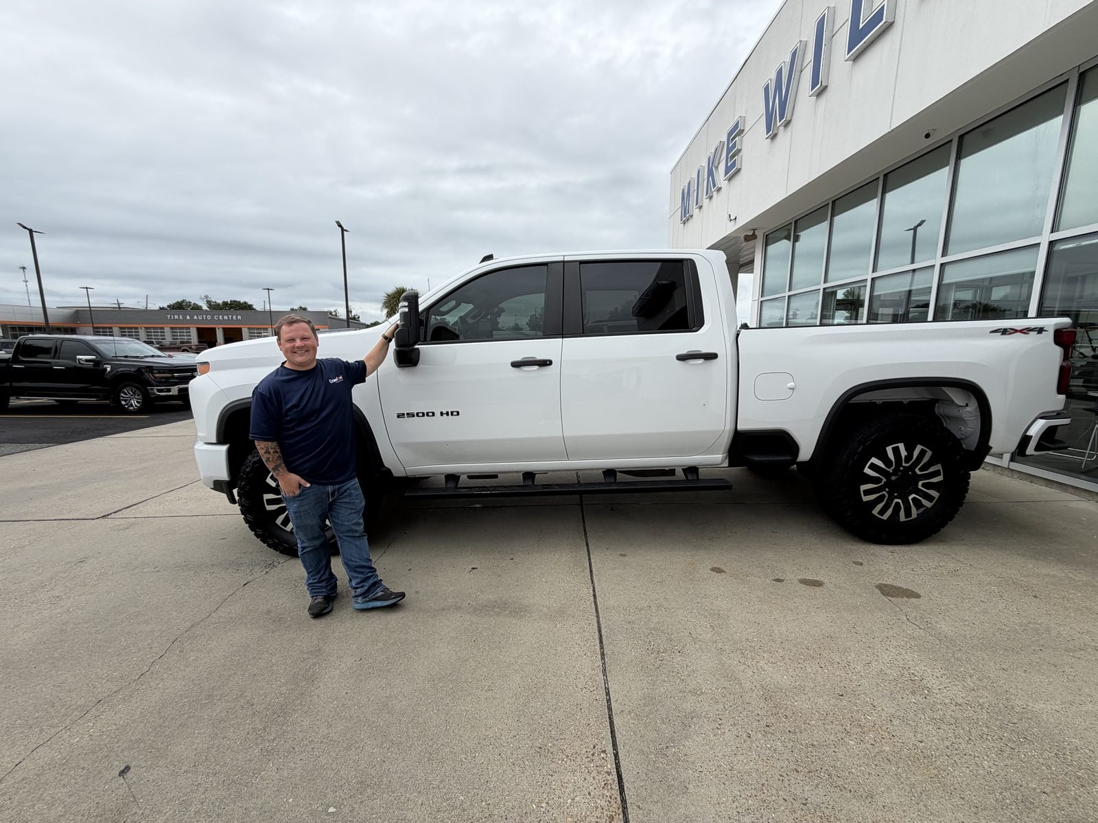 Owner standing with his white lifted 2021 Silverado 2500HD on 37-inch tires at a dealership